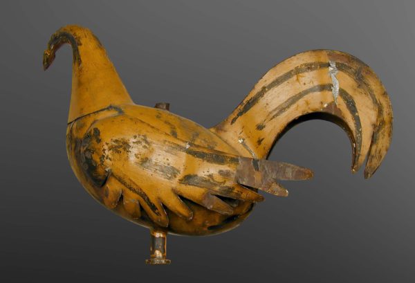 Le coq girouette est recouvert de peinture jaune écaillée. Là où la peinture est enlevée, on voit de la rouille.