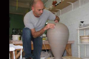 We can see the artist in his studio making a very large clay vase on a potter's wheel.
