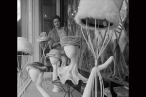 Photograph from the 1960s featuring mannequin heads displaying hats. A woman is looking at them.